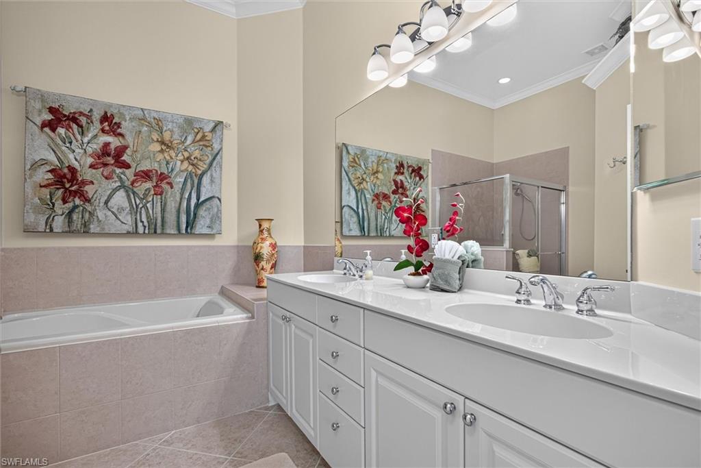 Bathroom featuring a dual vanity with white cabinetry and integrated sinks, a large mirror with overhead lighting, a built-in soaking tub, and a separate shower enclosure