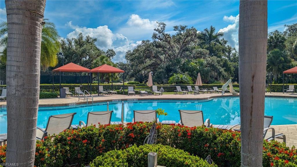 Expansive outdoor swimming pool with paver decking, multiple lounge chairs, and two red shade structures