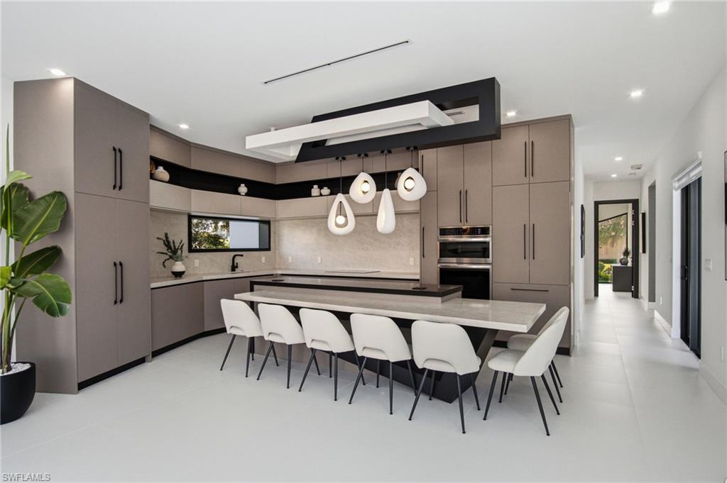 Modern kitchen featuring an expansive island with seating, integrated appliances, slab cabinetry, and a sleek linear lighting fixture