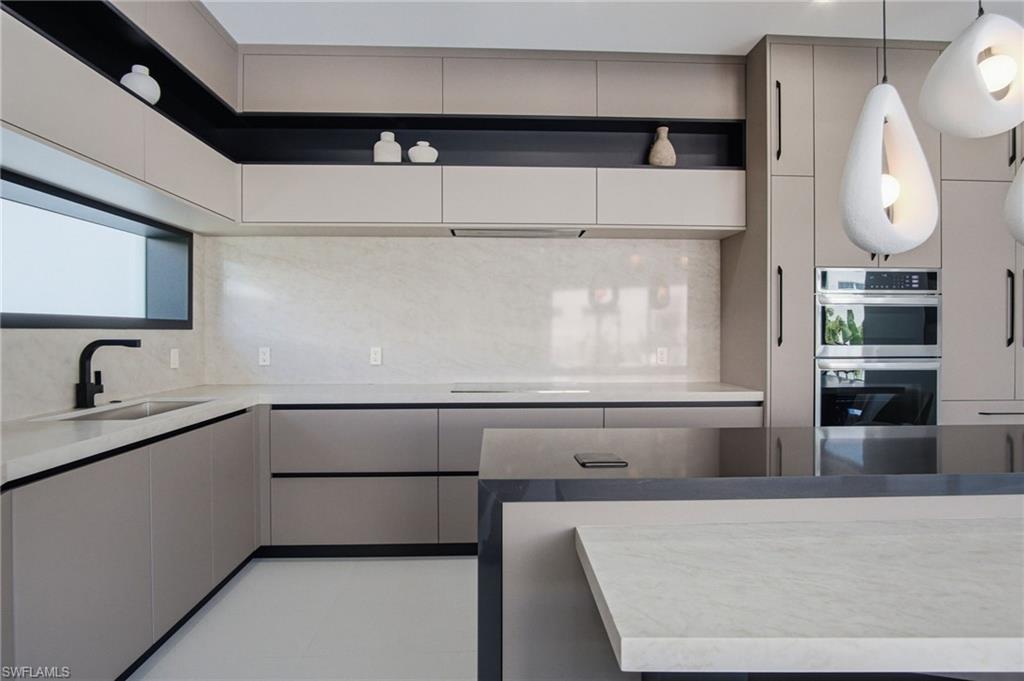 Modern kitchen featuring light-toned cabinetry with integrated hardware, a contrasting black accent shelf, and a light-colored countertop