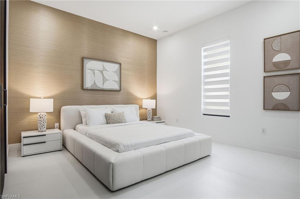 Spacious room featuring white flooring, a prominent accent wall with textured wallpaper, recessed lighting, a modern window treatment, and a dark-framed doorway