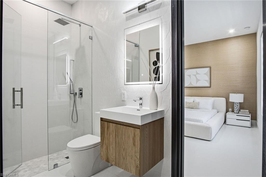Bathroom featuring a frameless glass shower enclosure, a wall-mounted vanity with wood-finish cabinetry, an illuminated mirror, and hexagonal tile flooring