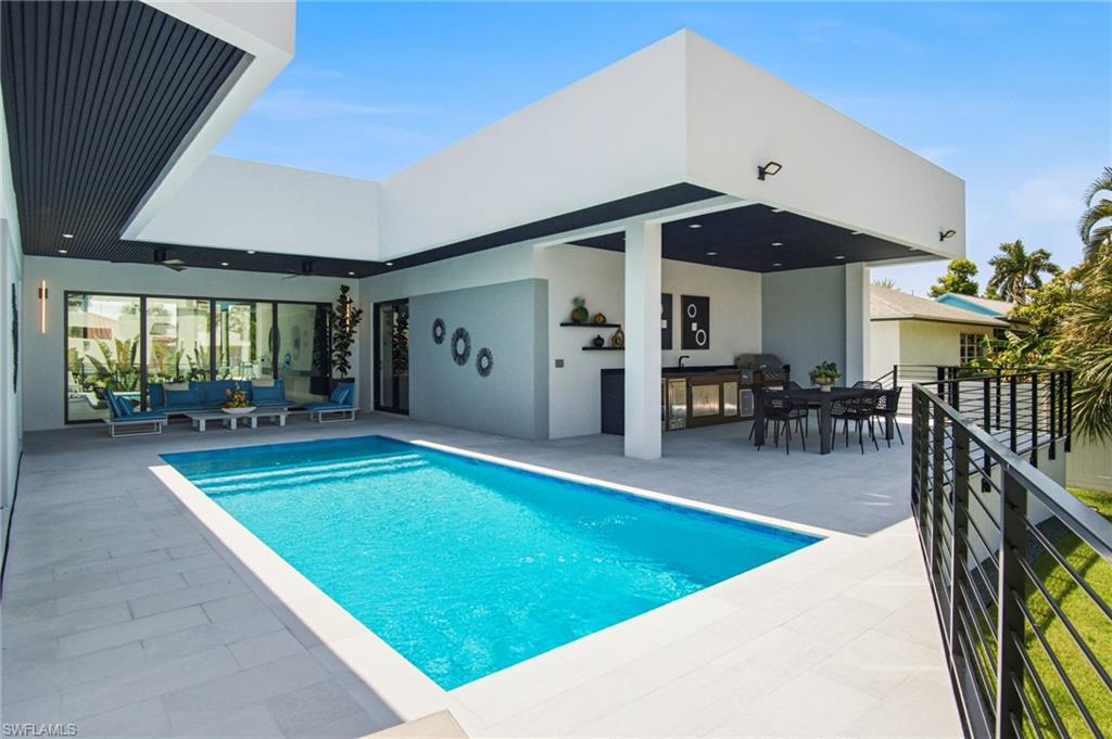 Outdoor living area featuring an integrated swimming pool, white tile surround, and a covered patio with an outdoor kitchen