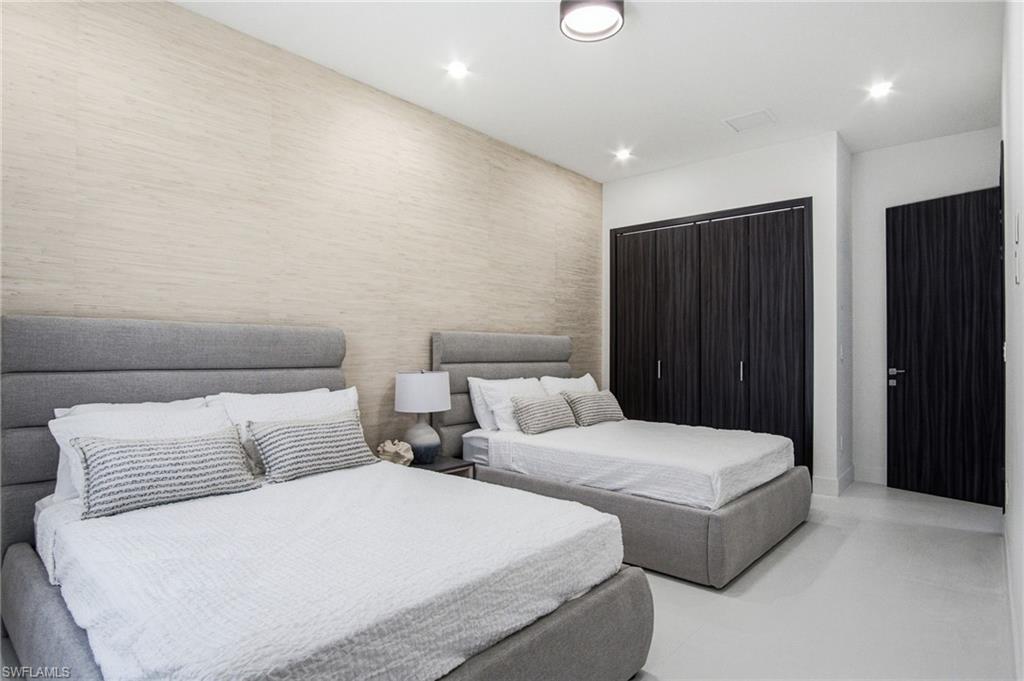 Room featuring textured accent wall, two upholstered bed frames, dark wood-finish bi-fold closet doors, and recessed lighting