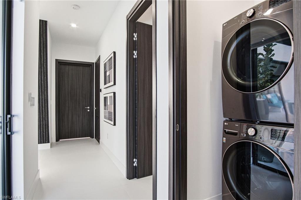 Integrated laundry area featuring a stacked washer and dryer, adjacent to a hallway with recessed lighting