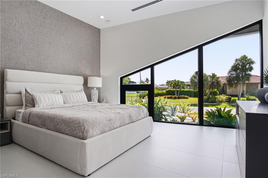 Expansive angled window wall with black framing, high ceilings with recessed lighting, textured accent wall, and large format light-toned floor tiles