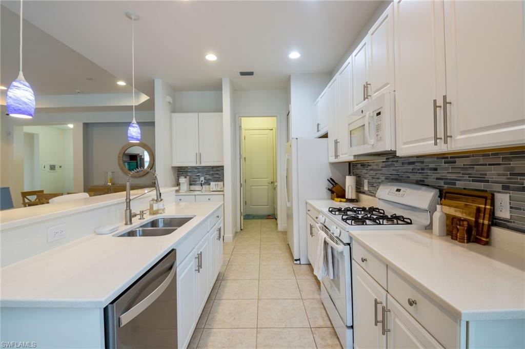 Modern kitchen featuring white cabinetry, light countertops, a tile backsplash, stainless steel sink, and pendant lighting