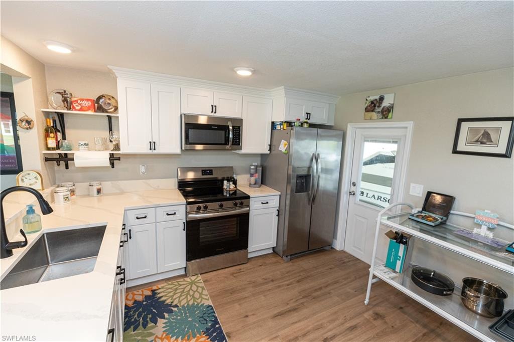 Kitchen featuring white cabinetry with dark hardware, a stainless steel appliance suite, white countertops, wood-finish flooring, and recessed lighting