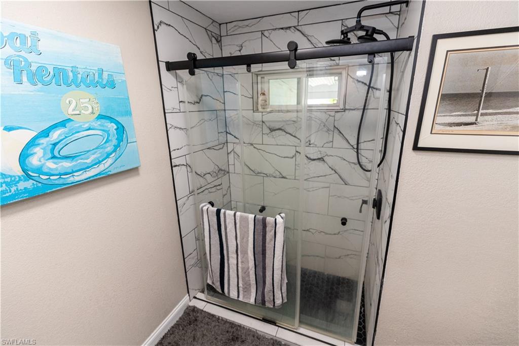 Glass-enclosed shower with black barn-door style hardware, white and gray marbled tile surround, black rainfall showerhead, and a rectangular window