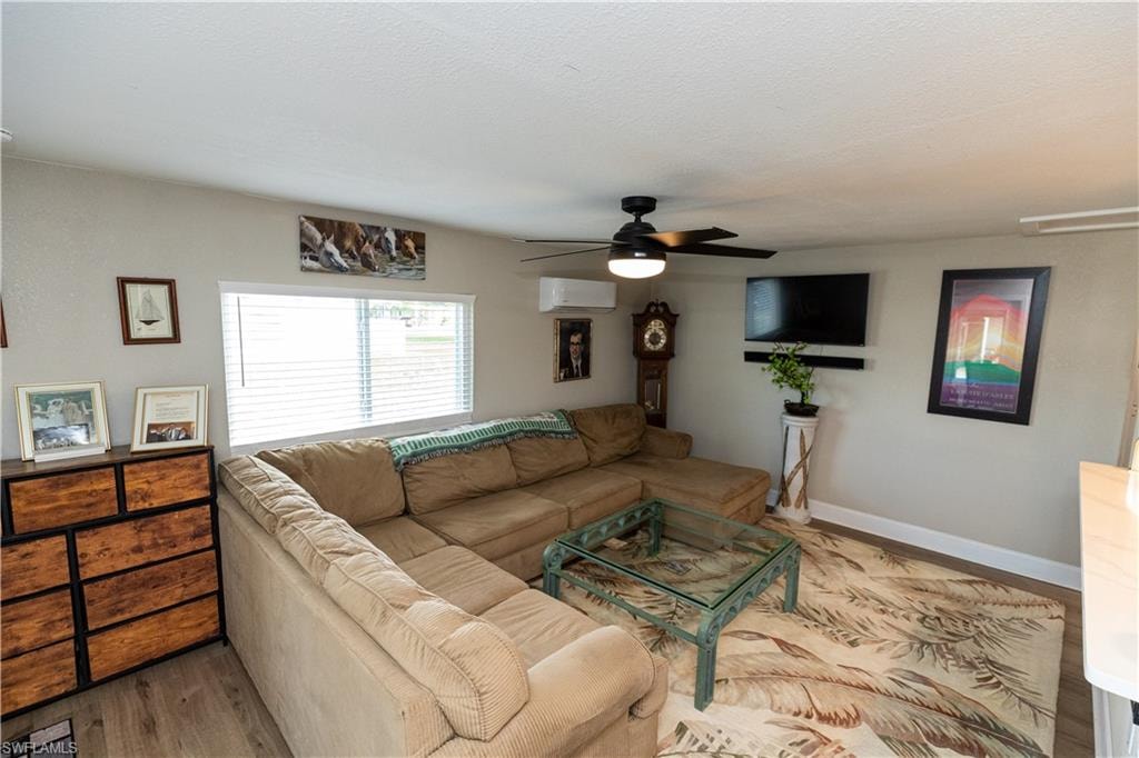 Living area featuring wood-finish flooring, a wall-mounted television, and a ceiling fan with integrated lighting