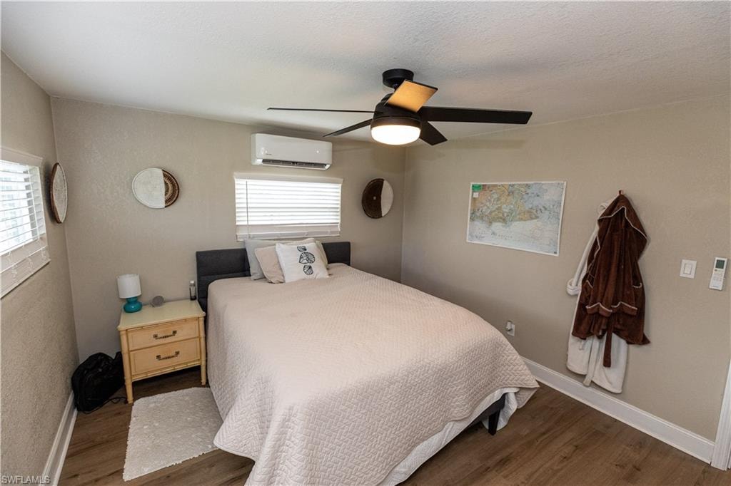 Bedroom featuring wood-finish flooring, a ceiling fan with integrated lighting, and a wall-mounted mini-split AC unit