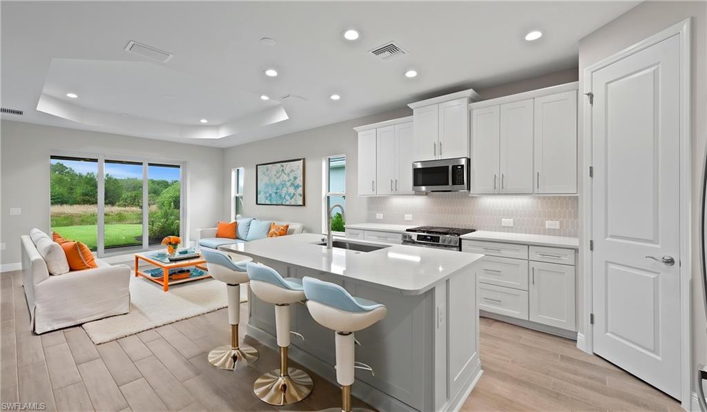 Open-concept kitchen featuring an island with seating, white shaker cabinetry, stainless steel appliances, and light-tone wood-finish flooring