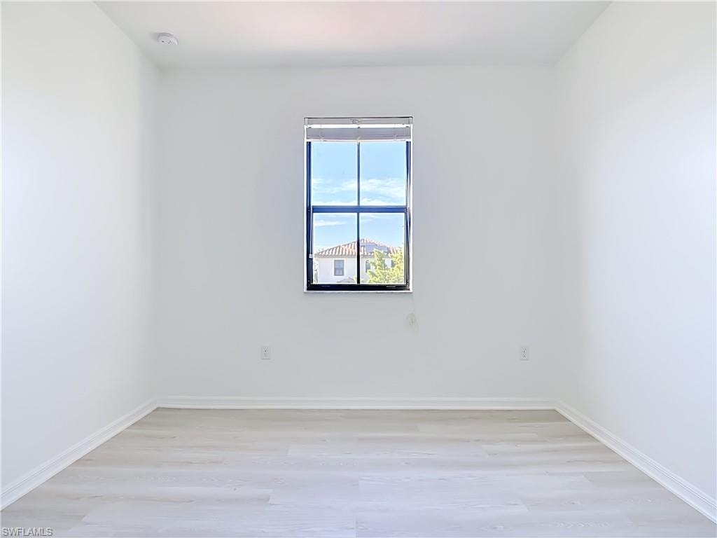 Bright interior space featuring a window with black trim, light wood-finish flooring, white baseboards, and neutral wall tones