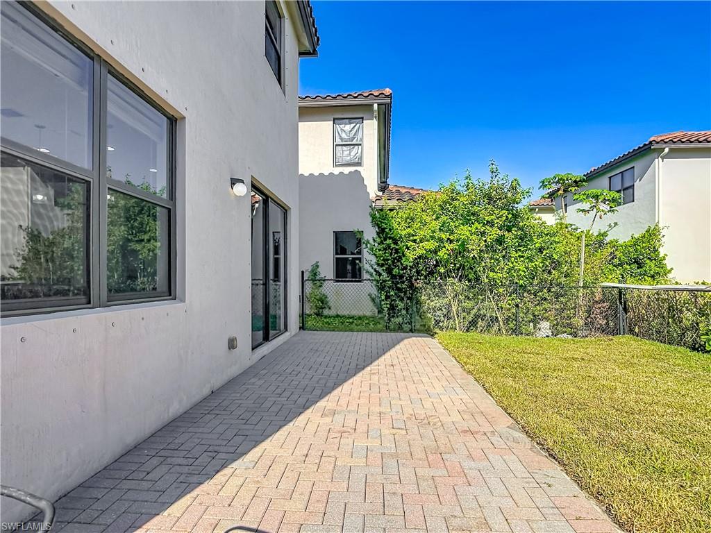 Outdoor paver patio with a grassy area and mature perimeter landscaping