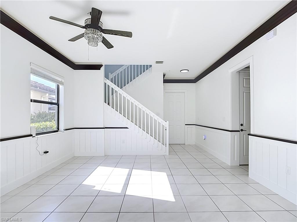 Expansive open-concept room featuring white tile flooring, beadboard wainscoting, and dark crown molding