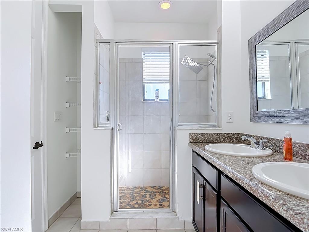 Bathroom featuring a glass-enclosed shower with mosaic tile flooring, dual undermount sinks, and a stone-finish countertop