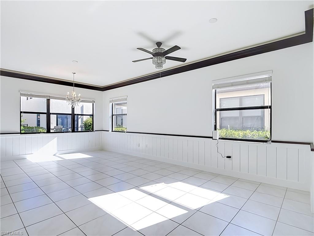 Spacious room featuring white tile flooring, white wainscoting, and dark crown molding