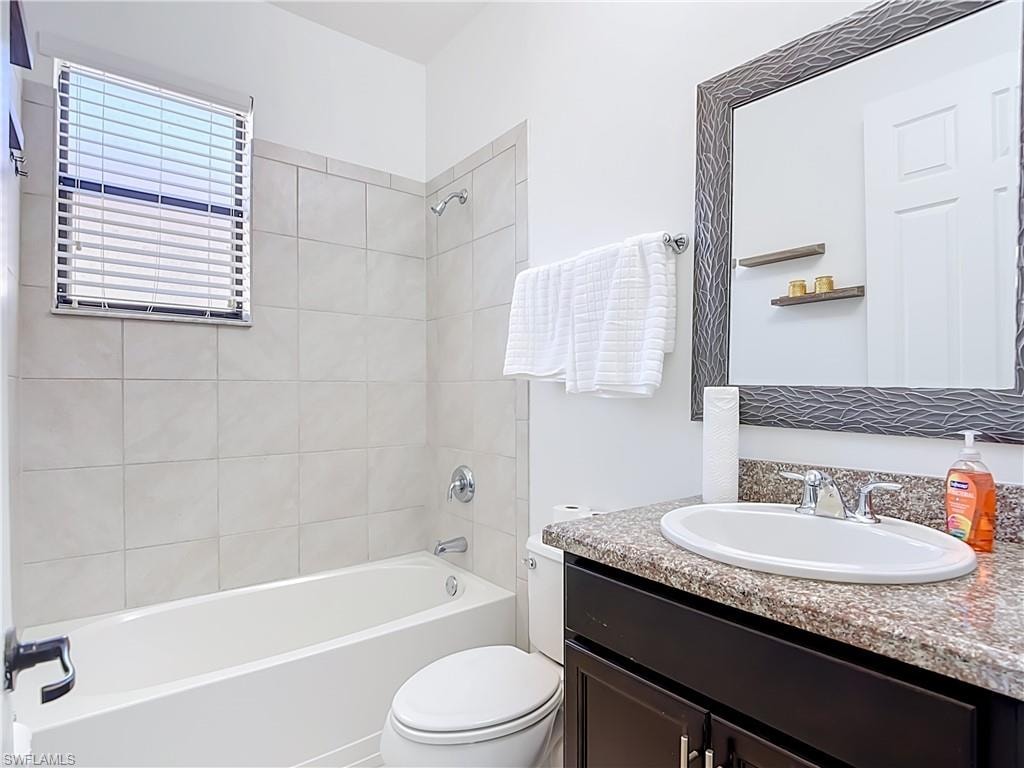 Bathroom featuring a tub/shower combination with tile surround, a single vanity with a granite-style countertop, a chrome faucet, and a large framed mirror