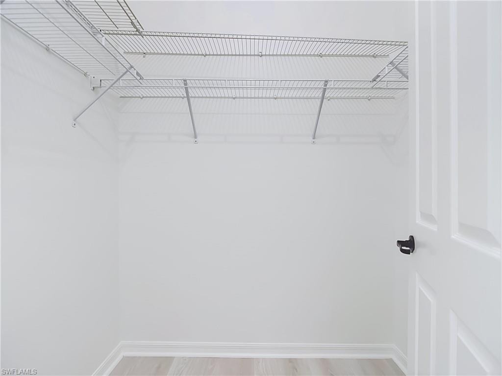 Spacious closet featuring wire shelving, bright white walls, light wood-finish flooring, and white baseboards