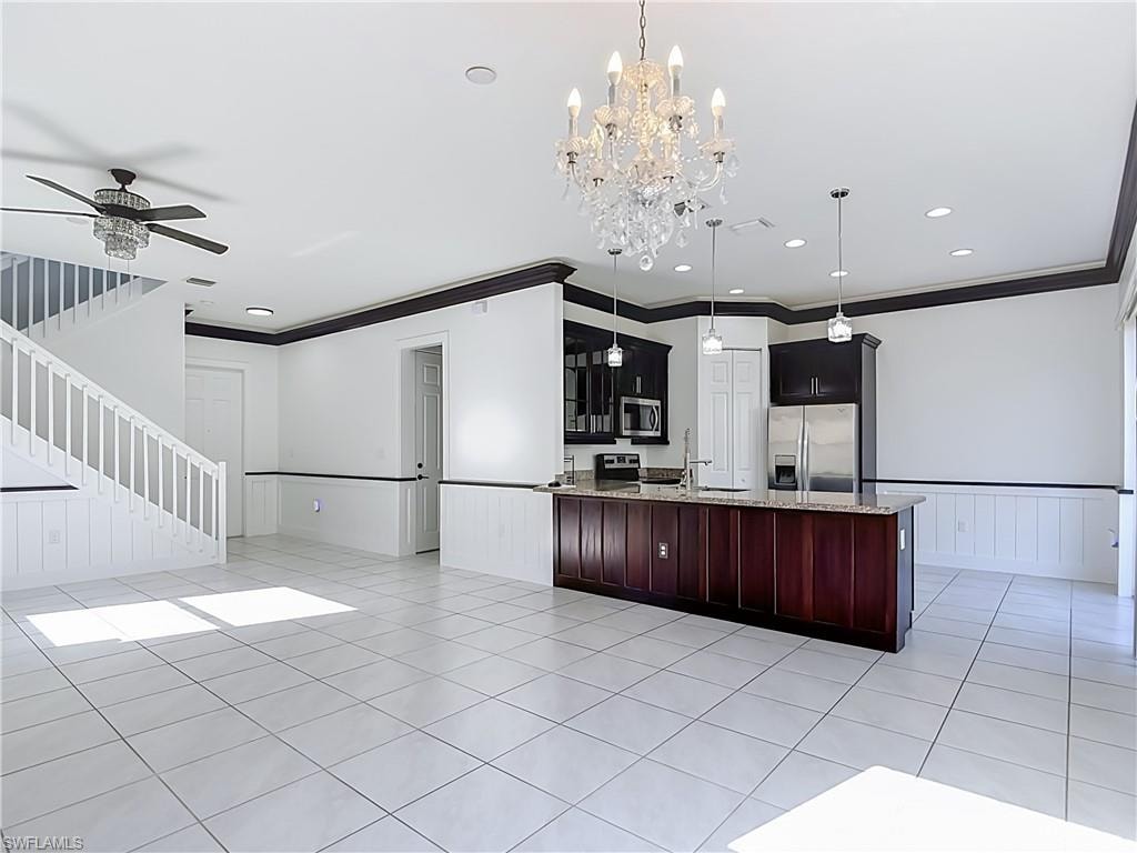 Open-concept kitchen and living area featuring white tile flooring, dark wood cabinetry, stainless steel appliances, and a central island with a granite-style countertop