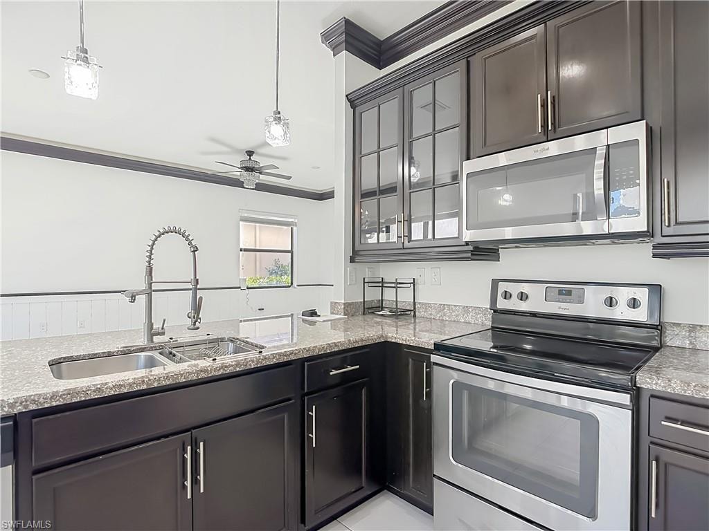 Modern kitchen featuring dark wood cabinetry, granite countertops, stainless steel appliances, a double basin sink with a high-arc faucet, and pendant lighting