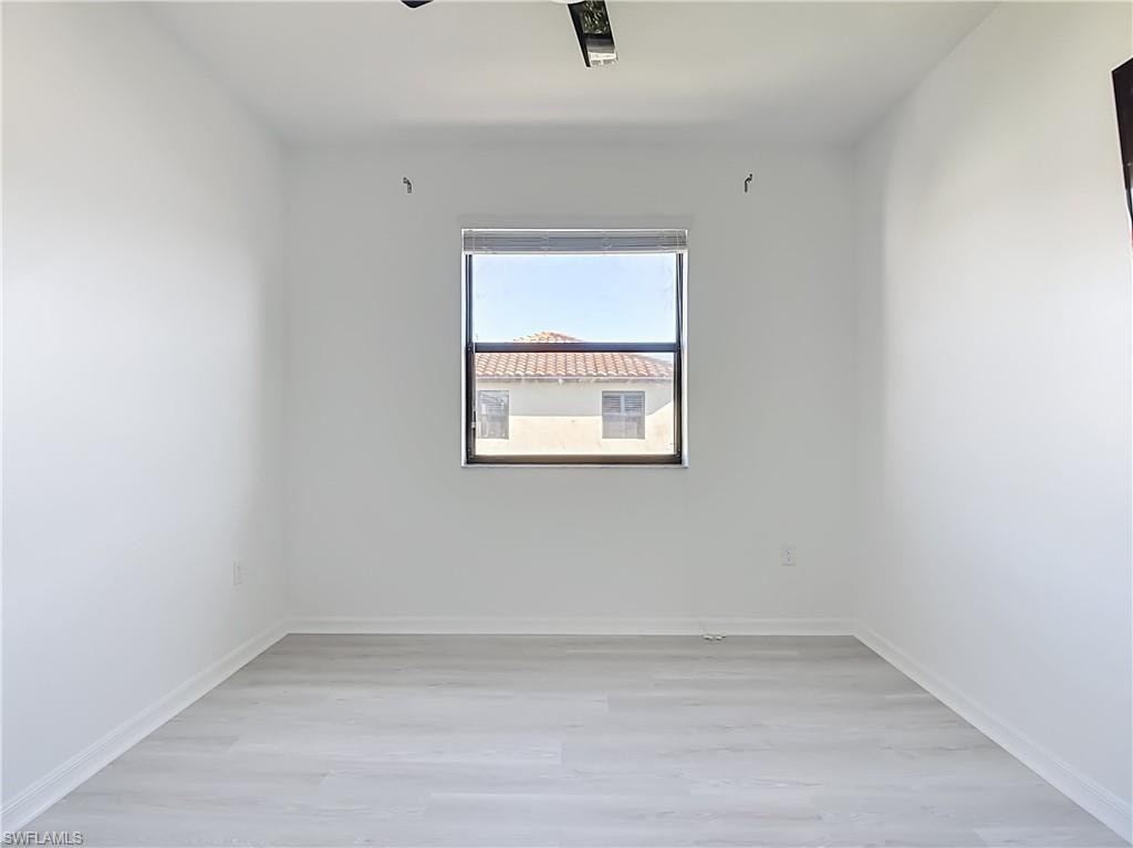 Bright room featuring a window with a dark frame, light wood-finish flooring, and crisp white walls