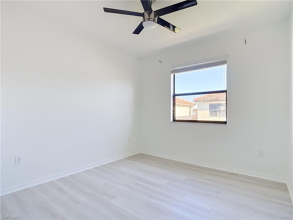 Room featuring light-toned wood-finish flooring, a window with exterior residential structures visible, and a ceiling fan with integrated lighting