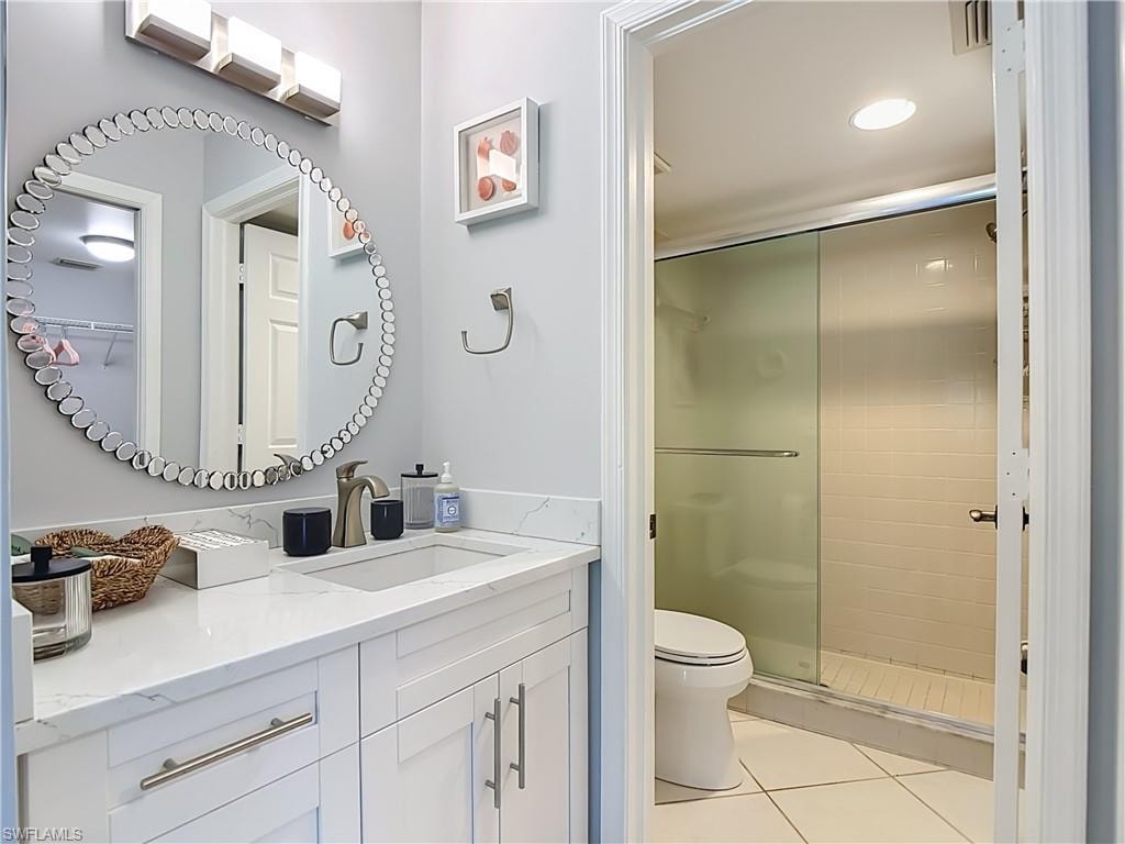 Bathroom featuring a vanity with a white countertop and rectangular sink, a circular mirror with a decorative frame, and a shower with a sliding glass door and white subway tile surround