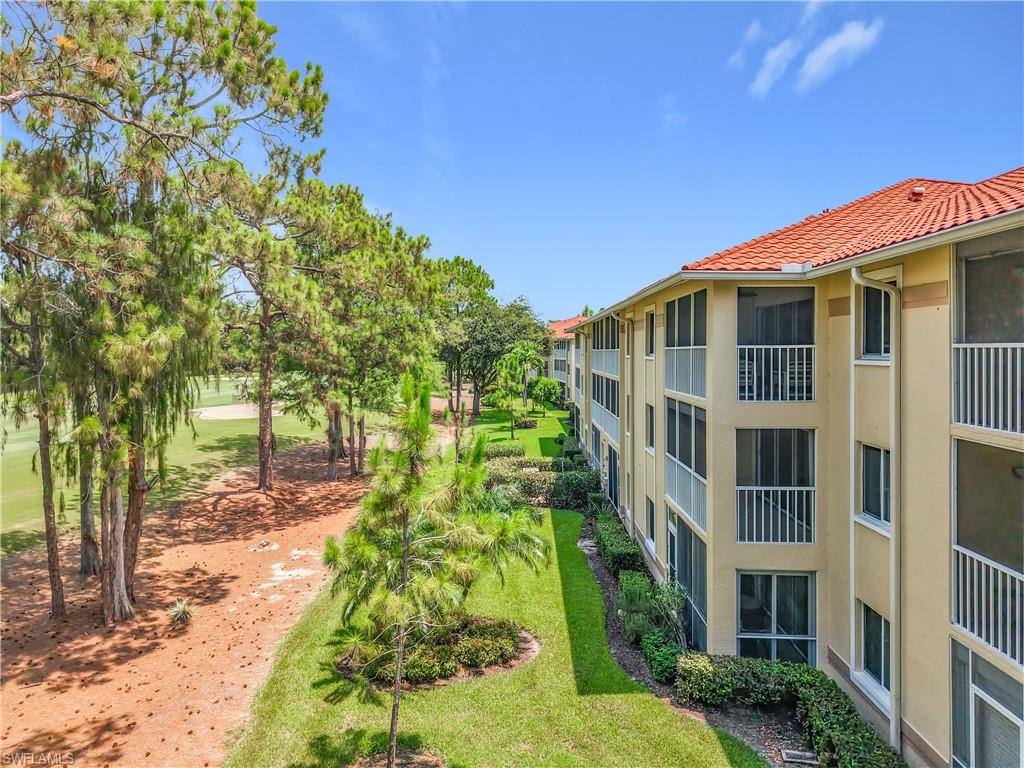 Exterior residential building featuring a terracotta tile roof, screened balconies with white railings, stucco siding, and a manicured lawn border