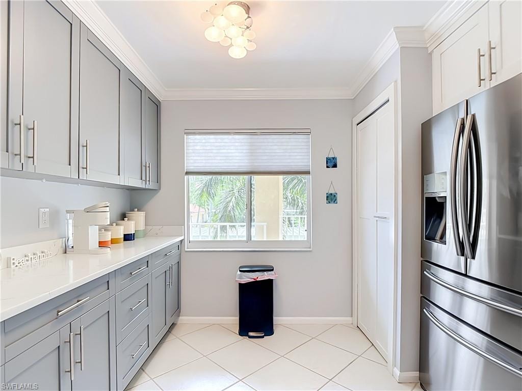 Modern kitchen featuring light gray cabinetry, white countertops, stainless steel refrigerator, and white tile flooring