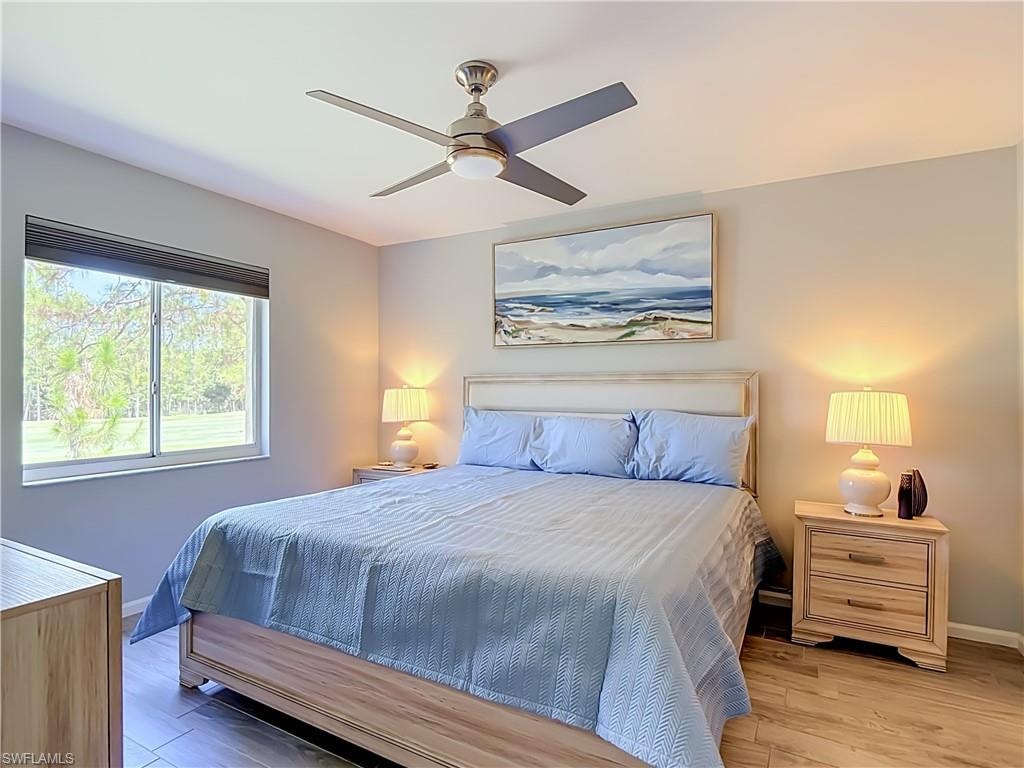 Bedroom featuring wood-finish flooring, a window with exterior landscaping, and a ceiling fan with integrated lighting
