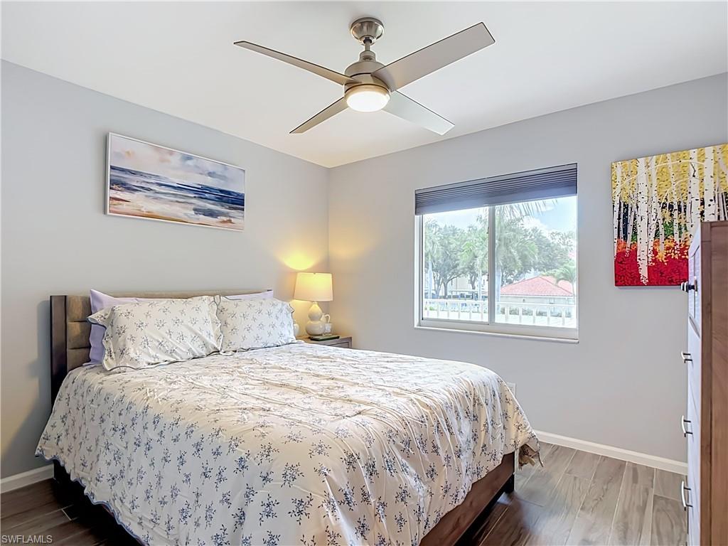 Bedroom featuring wood-finish flooring, a contemporary ceiling fan with integrated lighting, and a large window with blinds