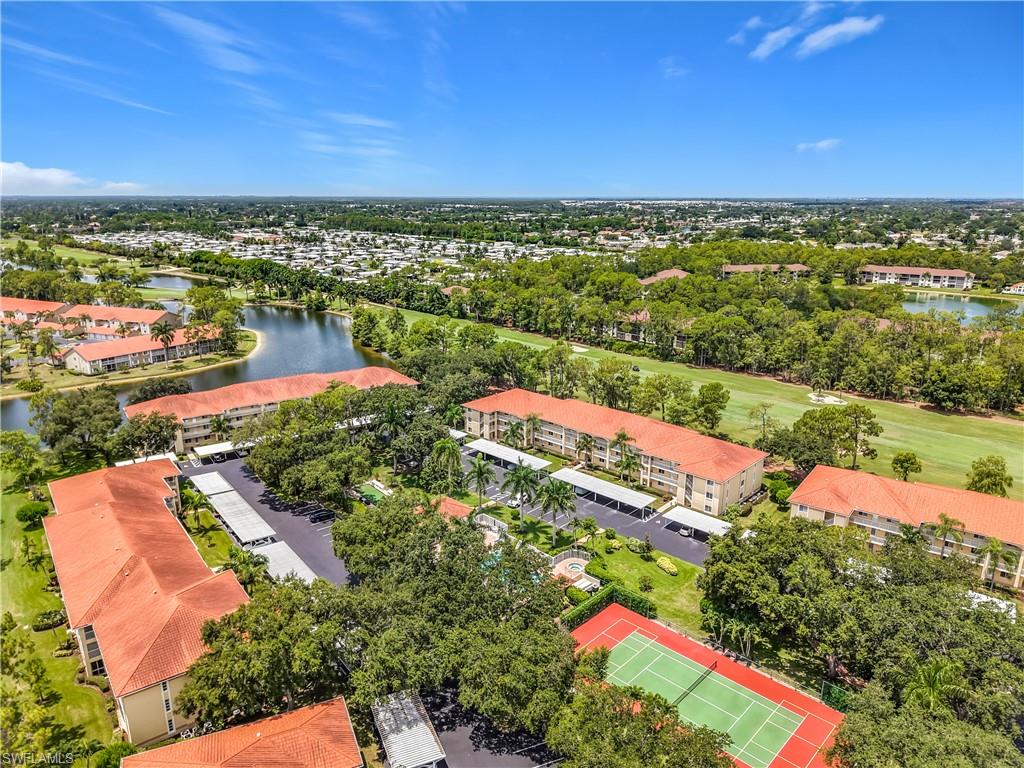 Expansive community featuring multiple buildings with tile roofs, a tennis court, swimming pool, and covered parking
