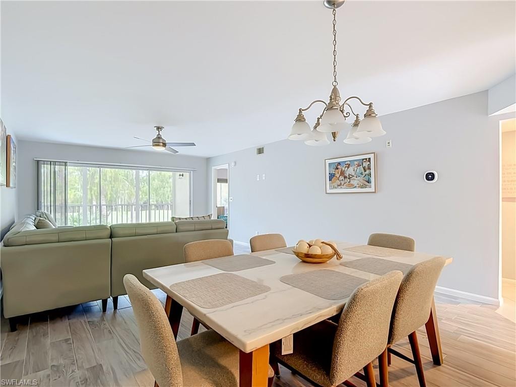 Dining area featuring a contemporary chandelier, light wood-finish flooring, and a sliding glass door with vertical blinds