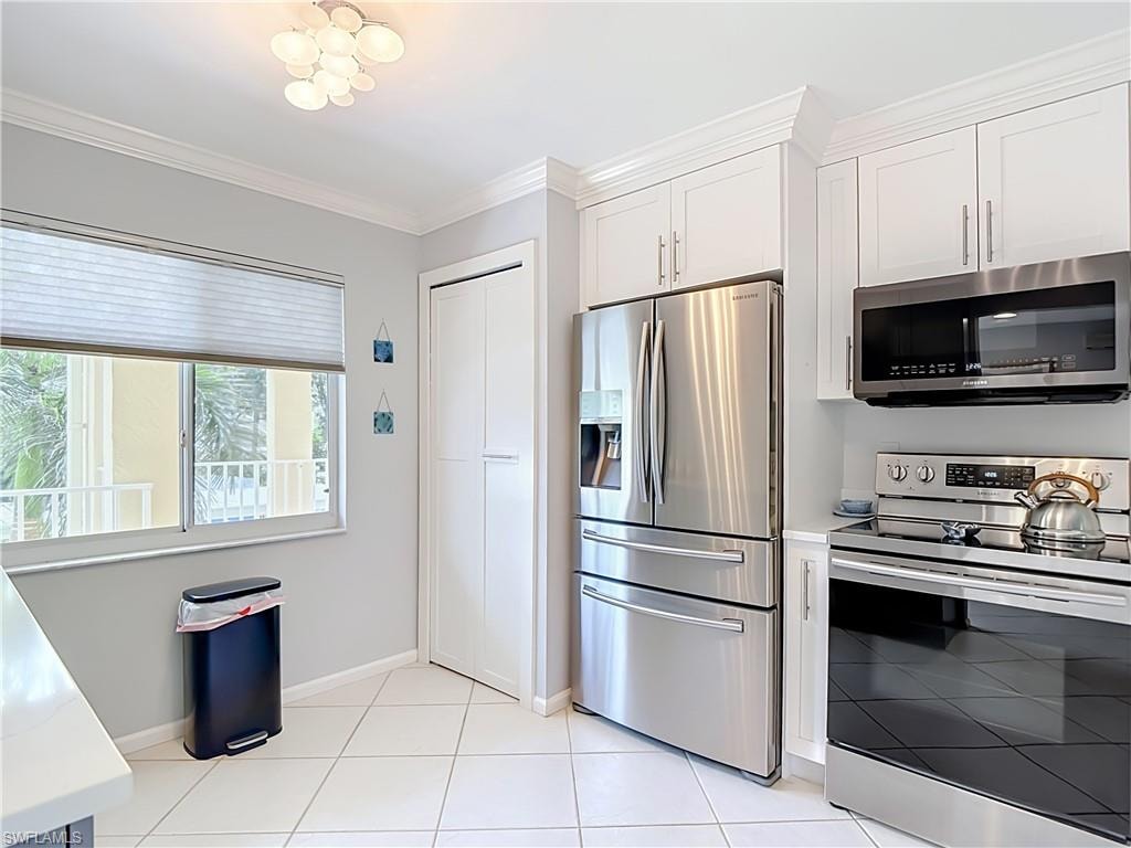 Kitchen featuring stainless steel appliances, white cabinetry with crown molding, white tile flooring, a built-in pantry, and a window with pleated blinds