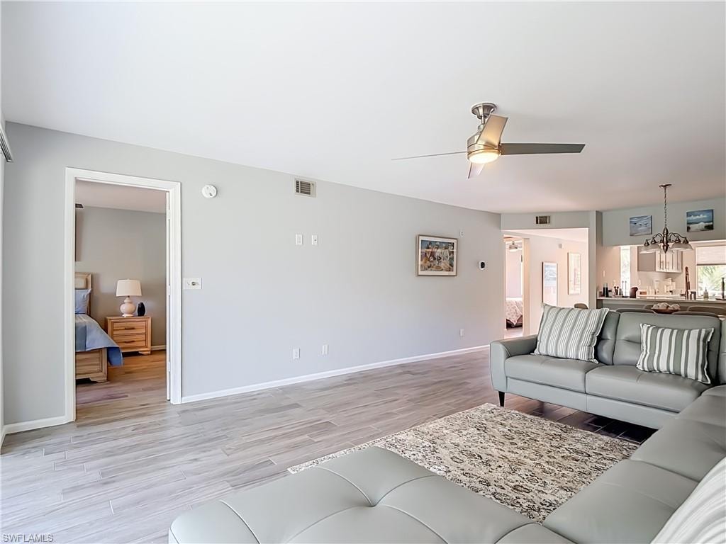 Spacious living area featuring wood-look tile flooring, light gray wall tones, and a ceiling fan with integrated lighting