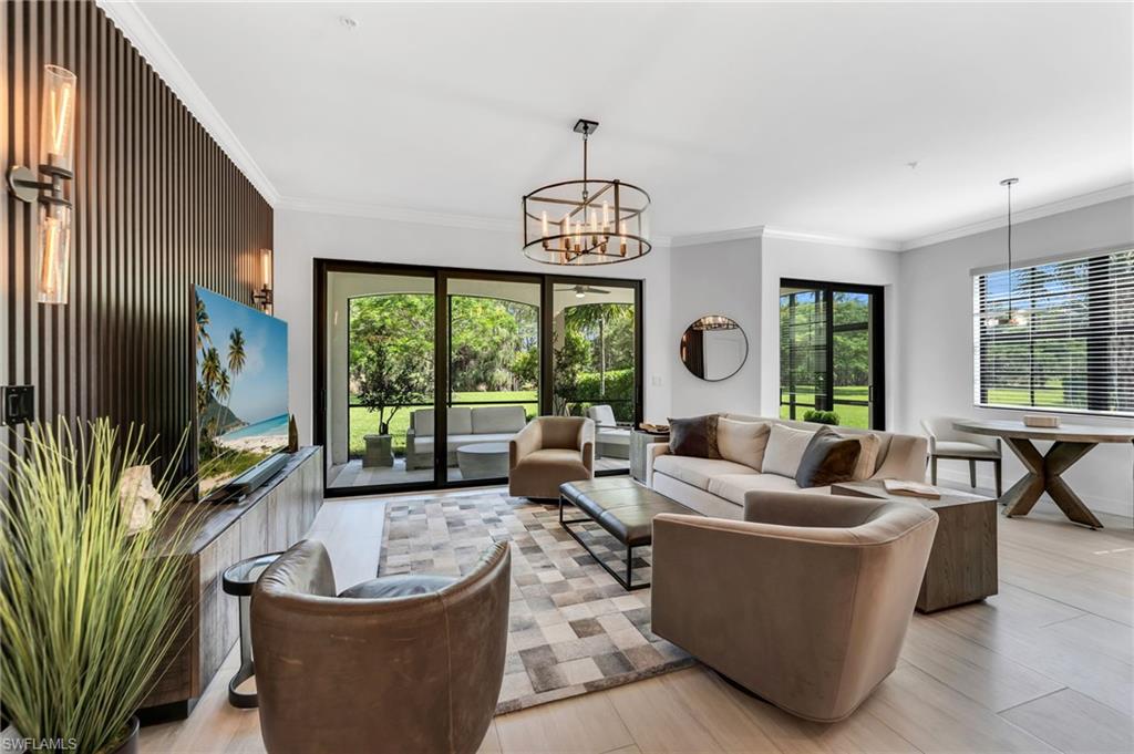 Spacious living area featuring light wood-finish flooring, a contemporary chandelier, recessed lighting, and a dark wood slat accent wall