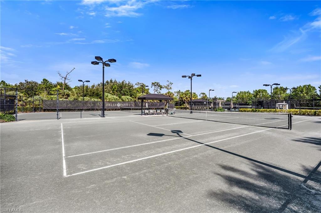 Multiple tennis courts with regulation nets and court lines, featuring perimeter fencing and overhead lighting