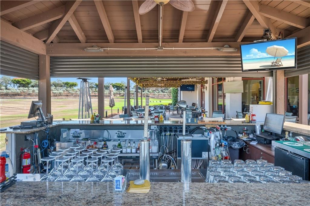 Outdoor bar area featuring an exposed beam ceiling, granite countertops, built-in shelving, and a mounted television