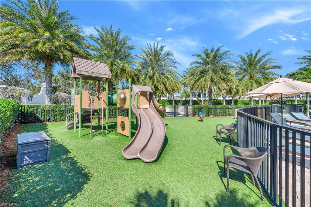 Recreational area featuring artificial turf, a multi-level play structure with slides, and mature palm trees
