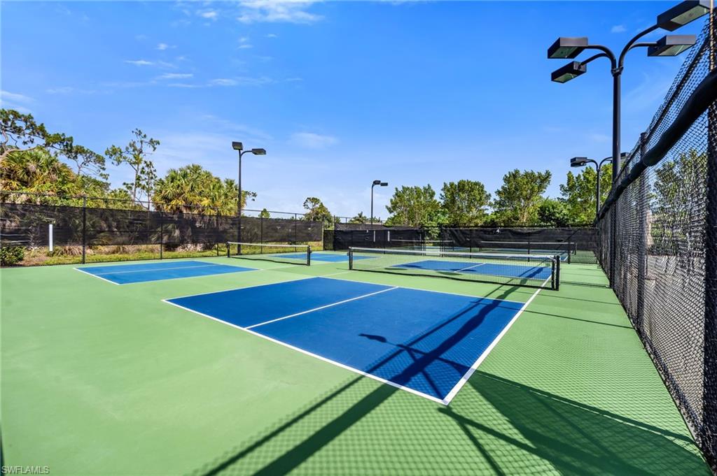 Multiple pickleball courts featuring a green and blue surface, perimeter fencing, and overhead lighting fixtures