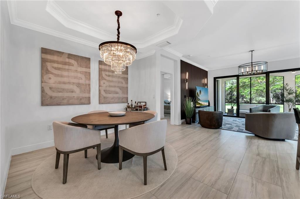 Dining area featuring a tiered crystal chandelier, tray ceiling, and light wood-finish flooring