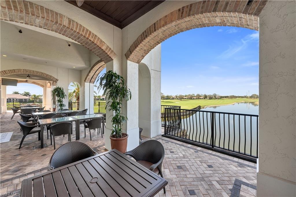 Covered outdoor patio featuring brick archways, paver flooring, and a black metal railing overlooking a body of water and a golf course