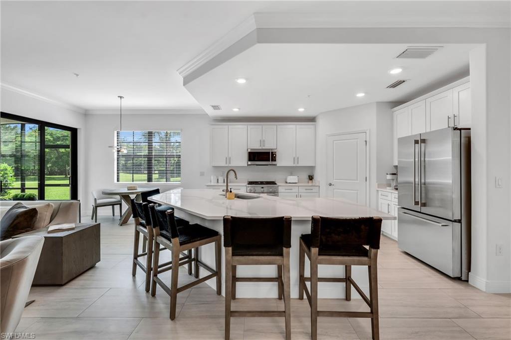 Contemporary kitchen featuring a large central island with seating, stainless steel appliances, abundant white cabinetry, and recessed lighting