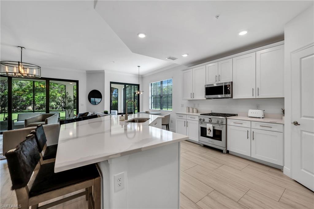 Expansive kitchen featuring a large island with a waterfall countertop, white shaker cabinetry, stainless steel appliances, and light wood-finish flooring