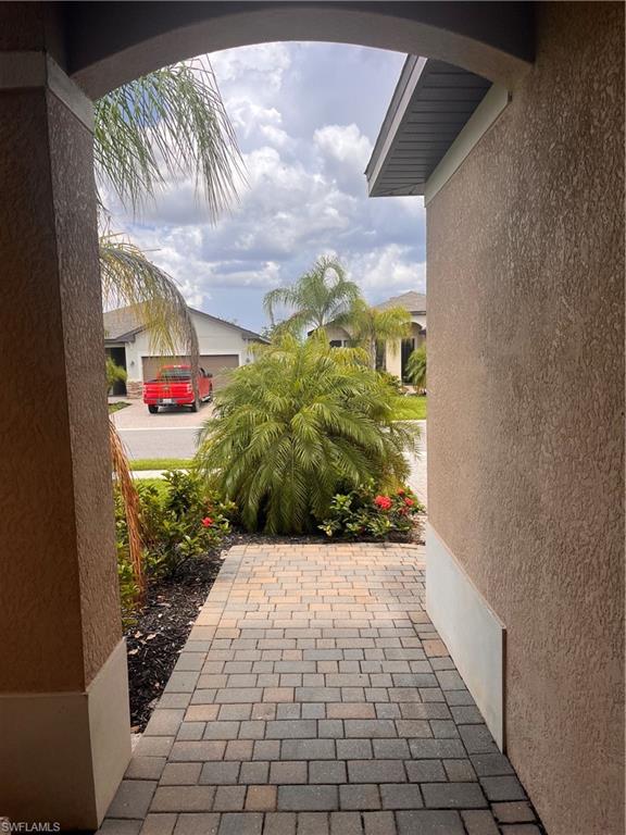 Entryway featuring a paver walkway, stucco exterior, and lush tropical landscaping