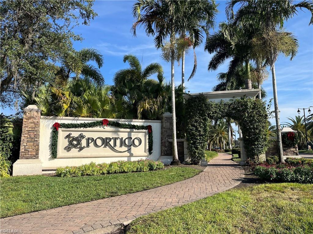 Stone-clad monument signage featuring "The Portico" lettering, surrounded by lush landscaping and mature palm trees