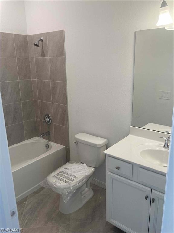 Full bathroom featuring a white tub, chrome shower fixtures, neutral wall tiling, a white vanity with integrated sink, and an overhead light fixture