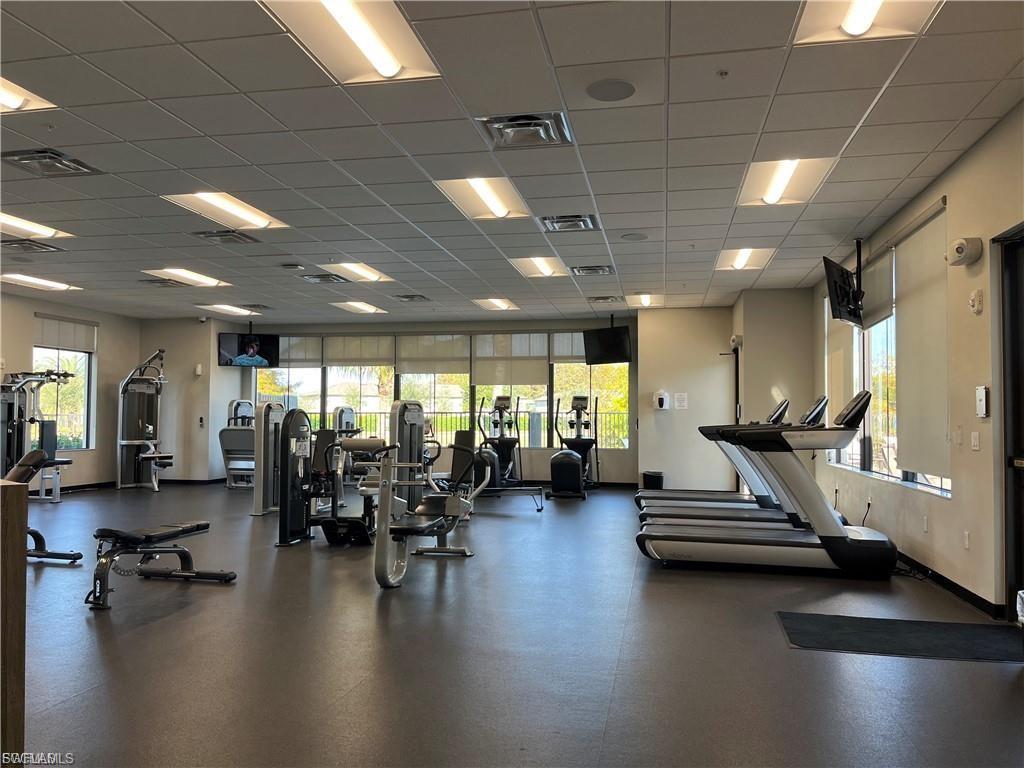 Spacious fitness center featuring a rubberized floor, multiple treadmills, strength training equipment, large windows with roller shades, and recessed lighting