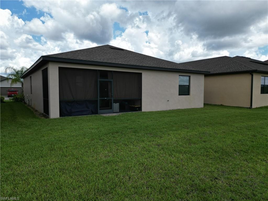 Expansive rear yard featuring a large screened-in patio, stucco exterior, dark roof shingles, and green lawn space